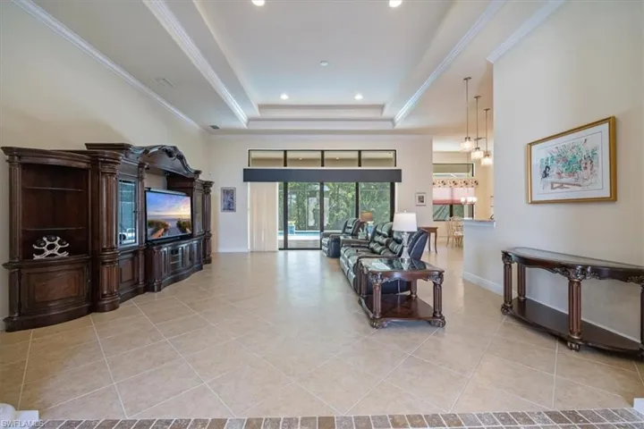 Living room with a tray ceiling, ornamental molding, light tile patterned floors, and recessed lighting