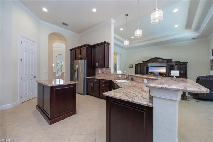 Kitchen featuring crown molding, arched walkways, open floor plan, dark brown cabinets, and stainless steel fridge