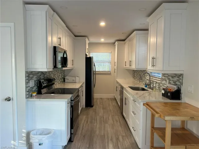 Kitchen with white cabinets, stainless steel appliances, light stone counters, light wood-type flooring, and recessed lighting