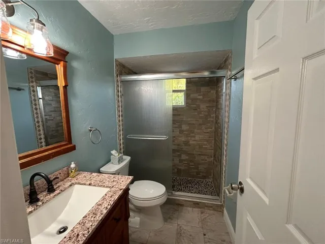 Full bathroom featuring vanity, a shower stall, a textured wall, a textured ceiling, and light marble finish floors