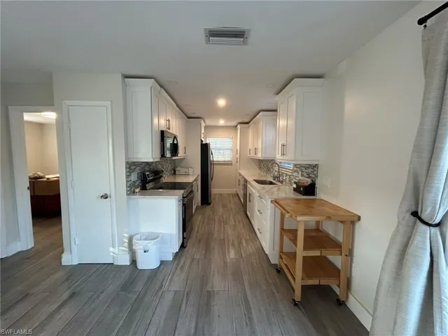 Kitchen featuring white cabinetry, stainless steel appliances, dark wood-style flooring, backsplash, and light stone countertops
