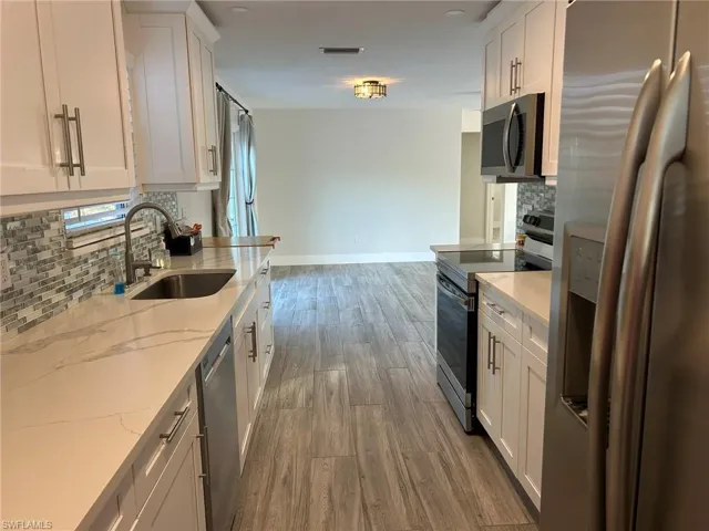 Kitchen featuring decorative backsplash, stainless steel appliances, white cabinetry, and light wood-style flooring