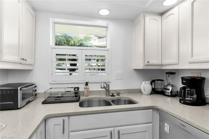 Kitchen with stainless steel dishwasher, light stone counters, and white cabinetry
