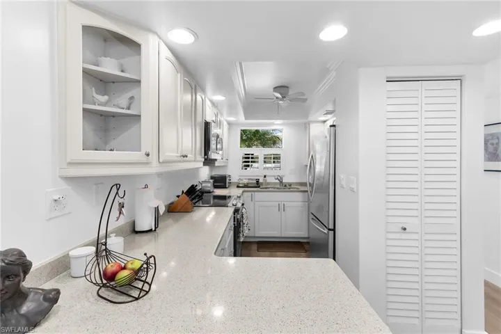 Kitchen featuring light stone countertops, white cabinets, crown molding, stainless steel appliances, and a ceiling fan