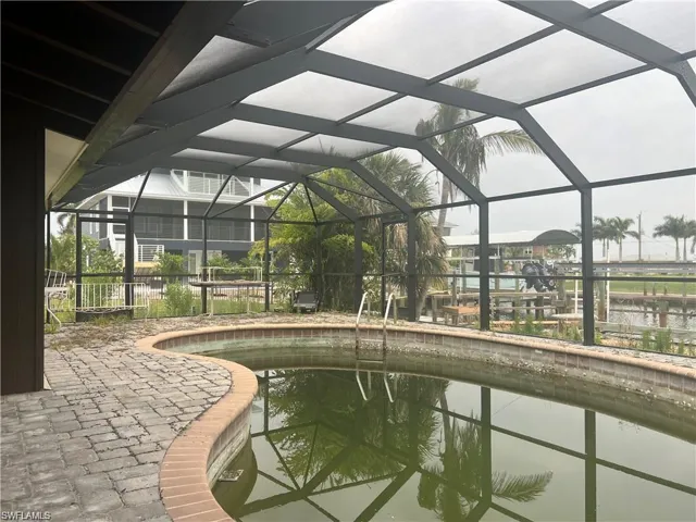Swimming pool featuring a water view, glass enclosure, and a patio