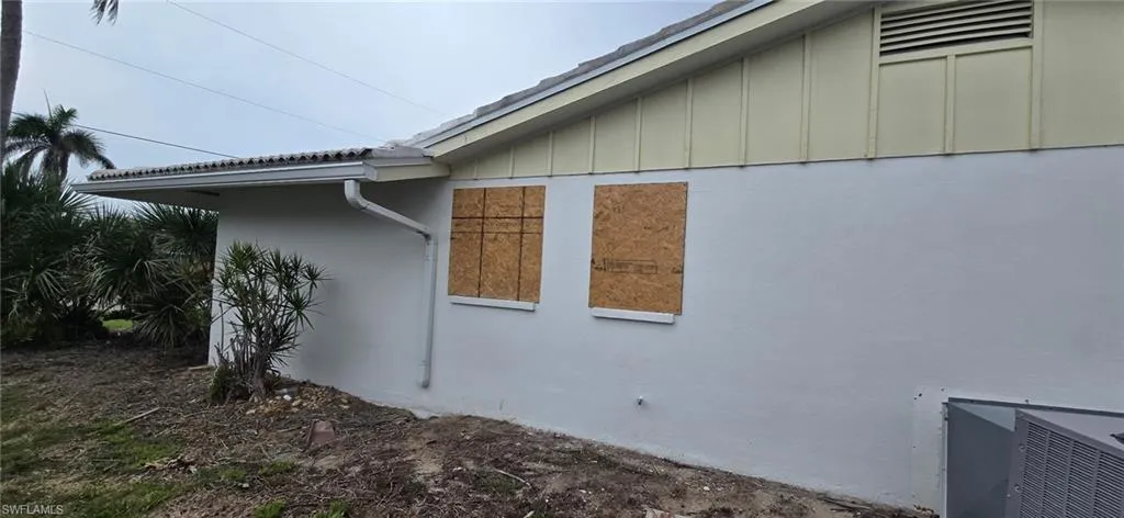 View of home's exterior featuring board and batten siding and stucco siding.  Home Boarded up as of 6/02/2025
