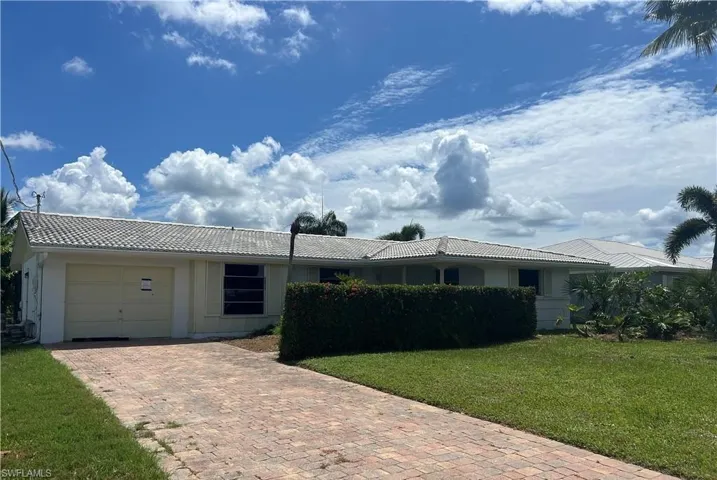 Ranch-style house with an attached garage, decorative driveway, a tile roof, and a front yard