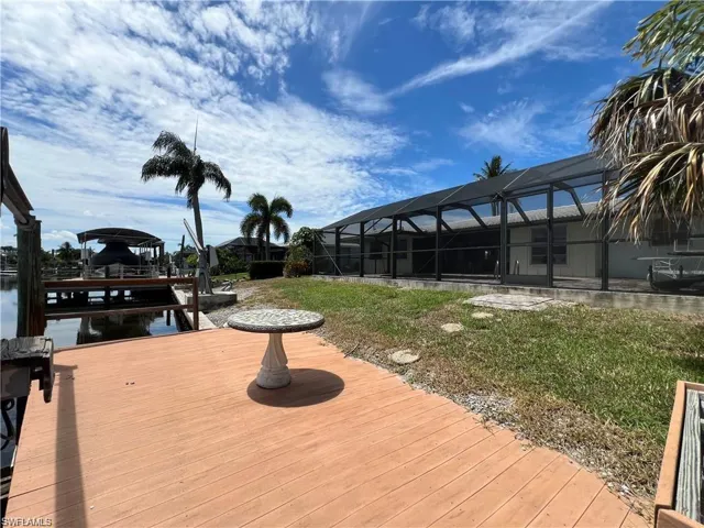 Wooden deck featuring a dock, a lanai, boat lift, and a yard