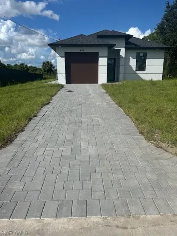 View of front facade featuring decorative driveway, an attached garage, a shingled roof, and a front yard