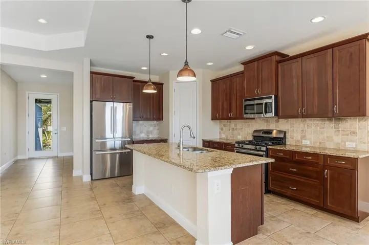 Large Kitchen with stainless steel appliances, light granite counters, tasteful backsplash, large kitchen island with sink, panty, and recessed and hanging lights.