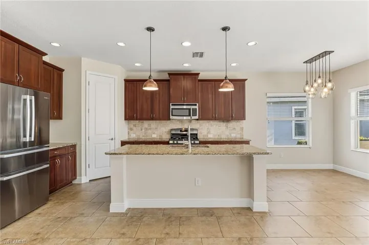 Large Kitchen with stainless steel appliances, light granite counters, tasteful backsplash, large kitchen island with sink, panty, and recessed and hanging lights.