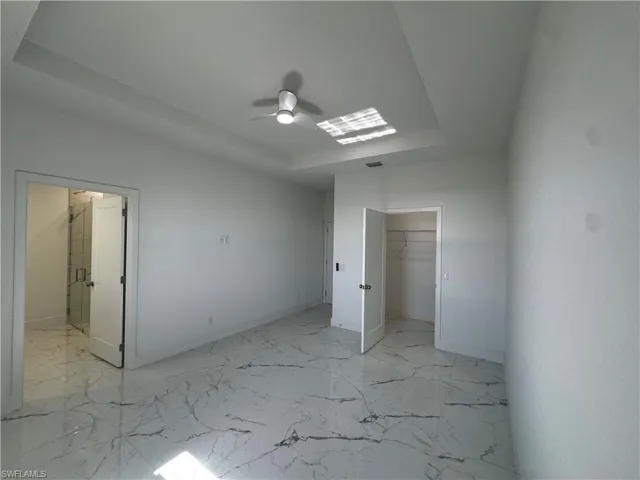 Master bedroom with baseboards, a raised ceiling, ensuite bathroom, marble finish floor, and a spacious closet