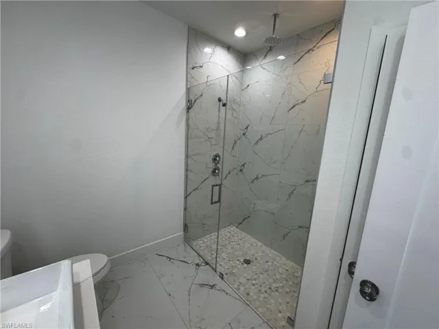 Full bath featuring a marble finish shower, marble finish floor, toilet, and baseboards