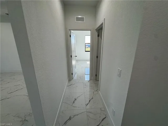 Second hallway with a textured wall, marble finish floor, visible vents, and baseboards