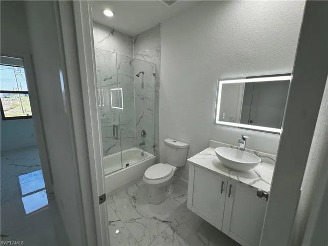 First bathroom with marble finish floor, toilet, combined bath / shower with glass door, vanity, and baseboards