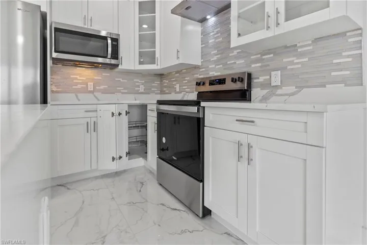 Kitchen with appliances with stainless steel finishes, tasteful backsplash, light marble finish flooring, and ventilation hood