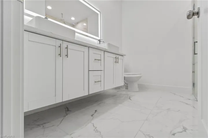 Full bathroom featuring marble look tiles, double vanity, recessed lighting, and a shower