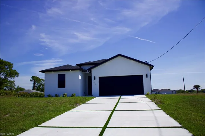 View of front facade featuring a garage, concrete driveway, a front lawn, and stucco siding