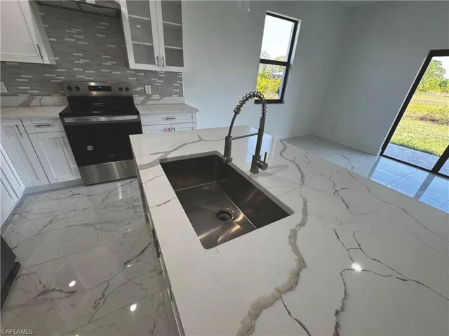 Kitchen featuring white cabinets, a sink, glass insert cabinets, and stainless steel range with electric cooktop