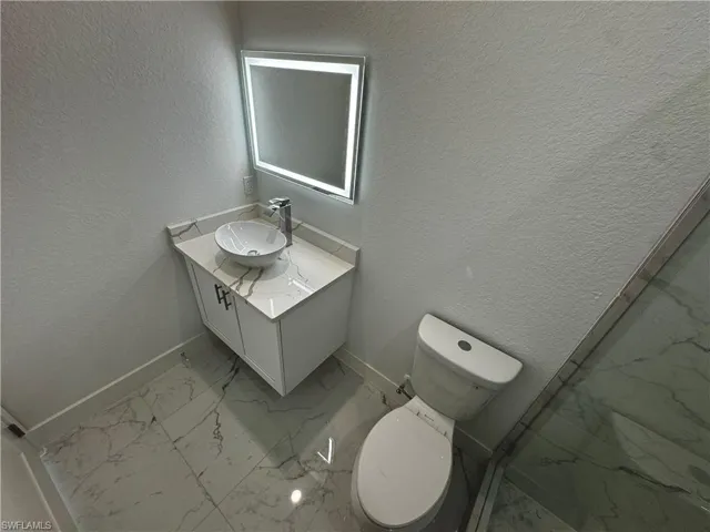 Master bathroom featuring a textured wall, marble finish floor, vanity, and baseboards