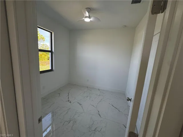 Second bedroom doorway with ceiling fan, marble finish floor, and baseboards
