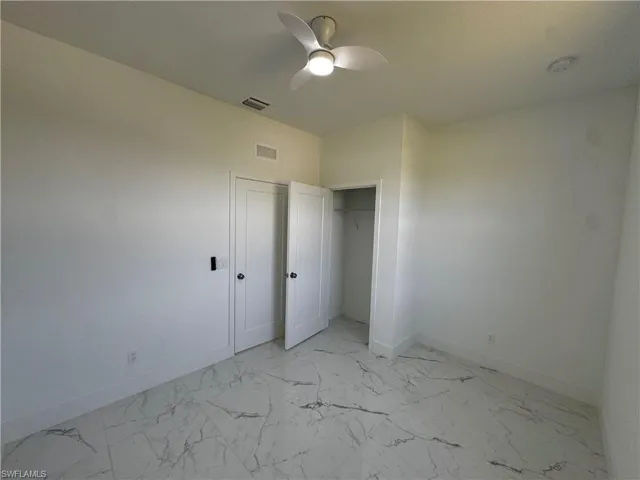 First bedroom featuring marble finish floor, a ceiling fan, visible vents, and baseboards