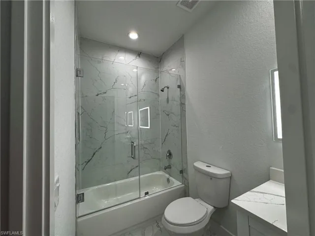 Full bath featuring a textured wall, marble finish floor, vanity, and visible vents