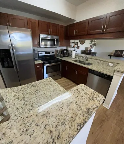 Kitchen with light stone counters, sink, dark wood-type flooring, and appliances with stainless steel finishes
