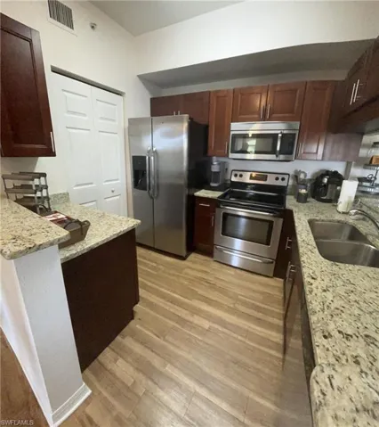 Kitchen with light hardwood / wood-style floors, sink, light stone countertops, and stainless steel appliances