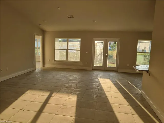 Tiled empty room with french doors, a healthy amount of sunlight, and baseboards