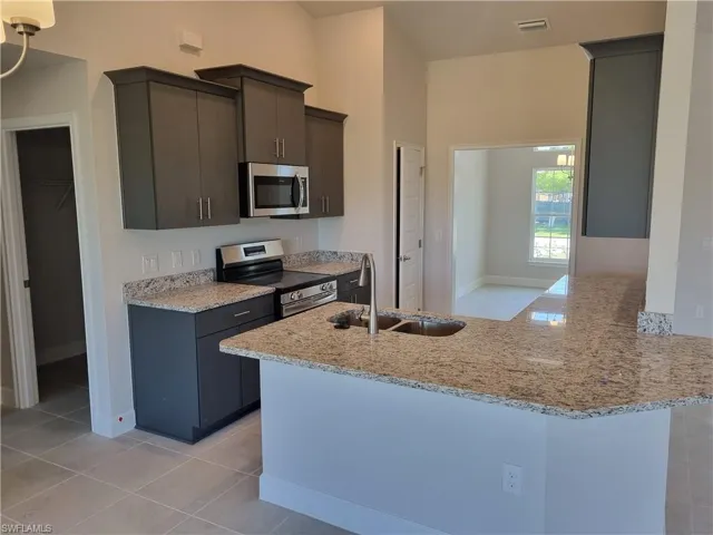 Kitchen featuring visible vents, a sink, light stone counters, appliances with stainless steel finishes, and a peninsula