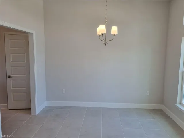 Spare room featuring light tile patterned floors, baseboards, and a chandelier