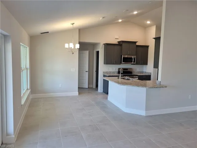 Kitchen with visible vents, lofted ceiling, light stone counters, appliances with stainless steel finishes, and an inviting chandelier
