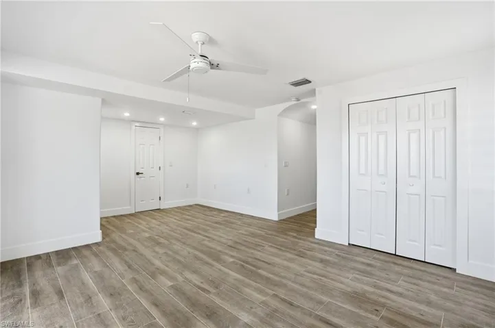 Unfurnished bedroom with arched walkways, light wood finished floors, recessed lighting, ceiling fan, and a closet - Virtually Edited Image