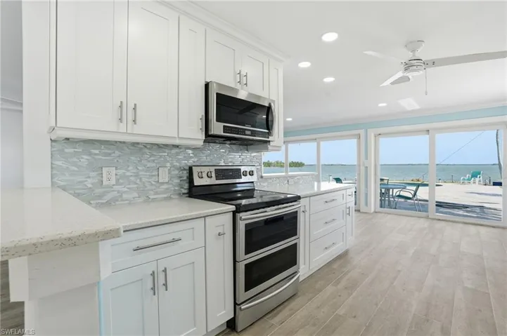 Kitchen with appliances with stainless steel finishes, crown molding, white cabinets, a water view, and recessed lighting - Virtually Edited Image