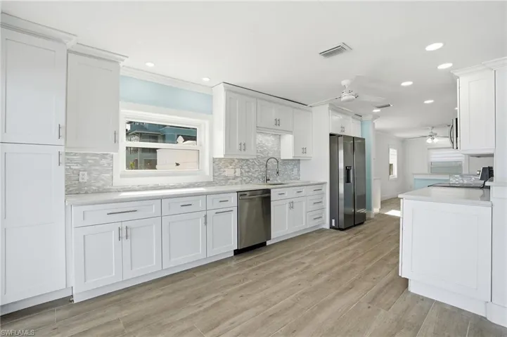 Kitchen with stainless steel appliances, a ceiling fan, white cabinetry, ornamental molding, and backsplash - Virtually Edited Image