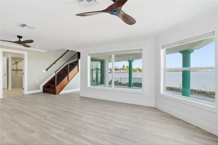 Unfurnished living room featuring ceiling fan, crown molding, stairs, light wood-style flooring, and a water view - Virtually Edited Image