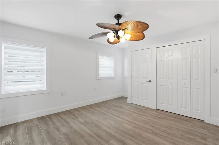 Unfurnished bedroom featuring light wood-style flooring, multiple windows, a ceiling fan, and a closet - Virtually Edited Image