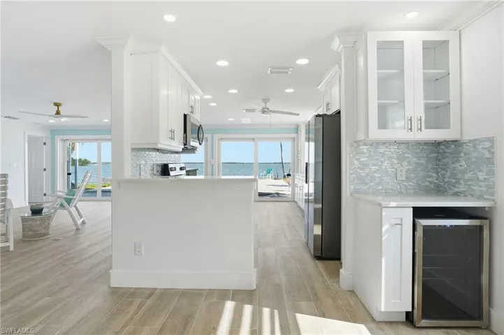 Kitchen with tasteful backsplash, white cabinets, wine cooler, and recessed lighting - Virtually Edited Image