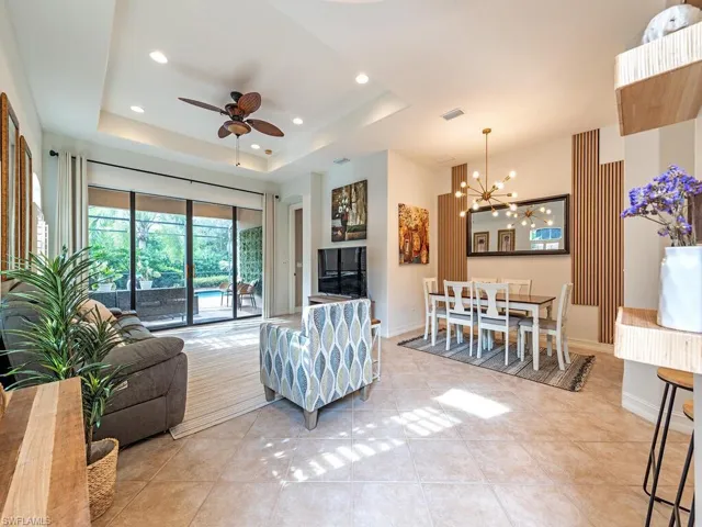 Tiled living room with ceiling fan with notable chandelier and a tray ceiling