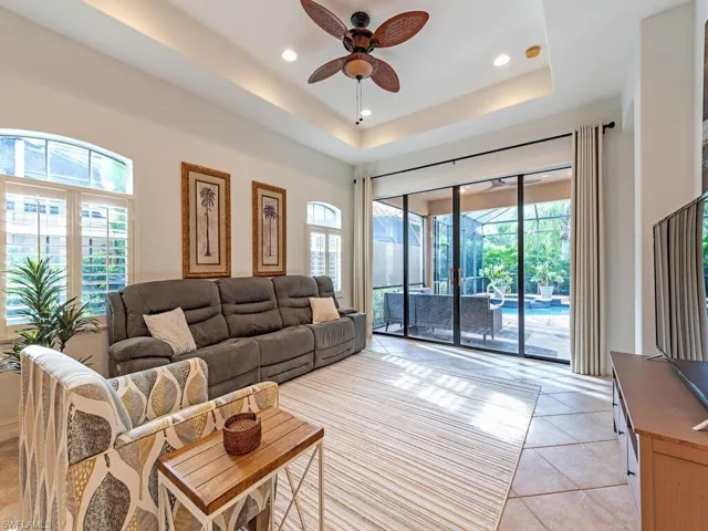 Living room featuring ceiling fan, light tile patterned flooring, a tray ceiling, and a healthy amount of sunlight