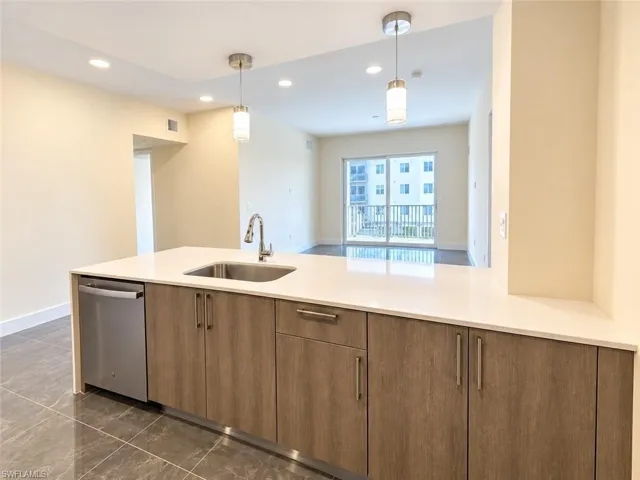 Kitchen island featuring a solid-surface countertop, stainless steel undermount sink, gooseneck faucet, flat-panel cabinetry, and integrated stainless steel dishwasher