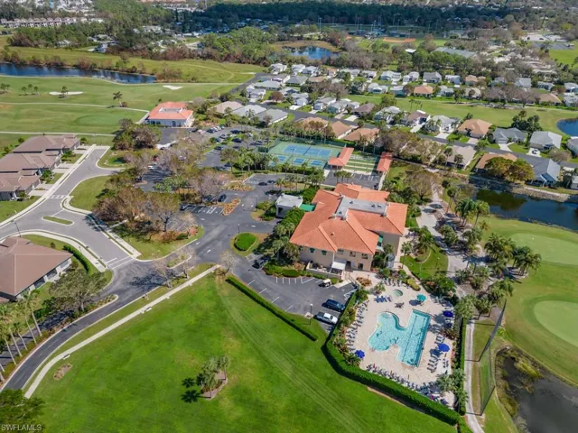 Aerial perspective of community facilities featuring an outdoor swimming pool, tennis courts, paved parking area, and surrounding golf course grounds