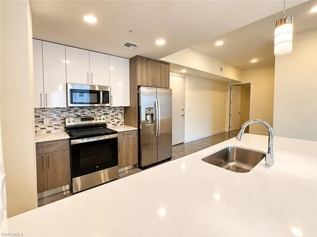 Kitchen featuring white gloss upper cabinetry, wood-finish lower cabinetry, solid-surface countertops, stainless steel appliances, and a mosaic tile backsplash
