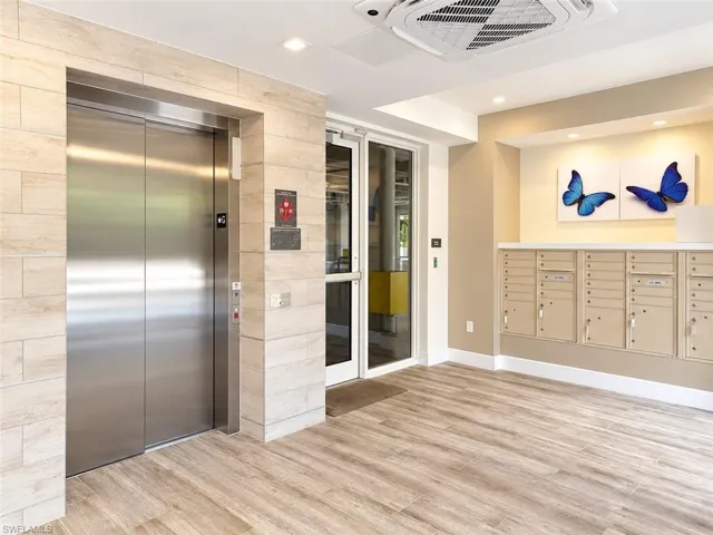Stainless steel elevator, tiled feature wall with wood-finish tile accents, integrated mail center, recessed ceiling lighting, and wood-finish flooring