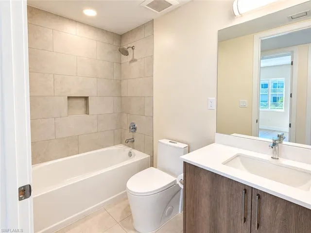 Bathroom featuring a wood-finish vanity with a solid-surface countertop, an undermount sink, a tub-shower combination with floor-to-ceiling tile surround, and a recessed wall niche
