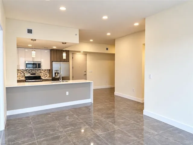 Kitchen featuring glossy white upper cabinetry, stone-finish tile backsplash, stainless steel appliances, breakfast bar, and polished tile flooring throughout
