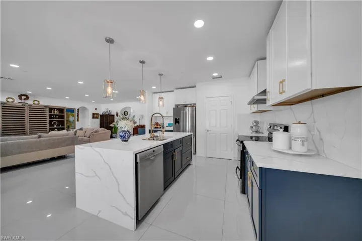 Kitchen with stainless steel appliances, light stone countertops, open floor plan, white cabinetry, and pendant lighting