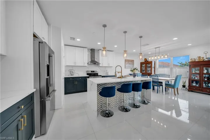 Kitchen with white cabinets, a kitchen breakfast bar, an island with sink, appliances with stainless steel finishes, and light stone counters