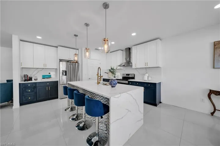 Kitchen featuring white cabinets, pendant lighting, light tile patterned floors, appliances with stainless steel finishes, and a kitchen breakfast bar